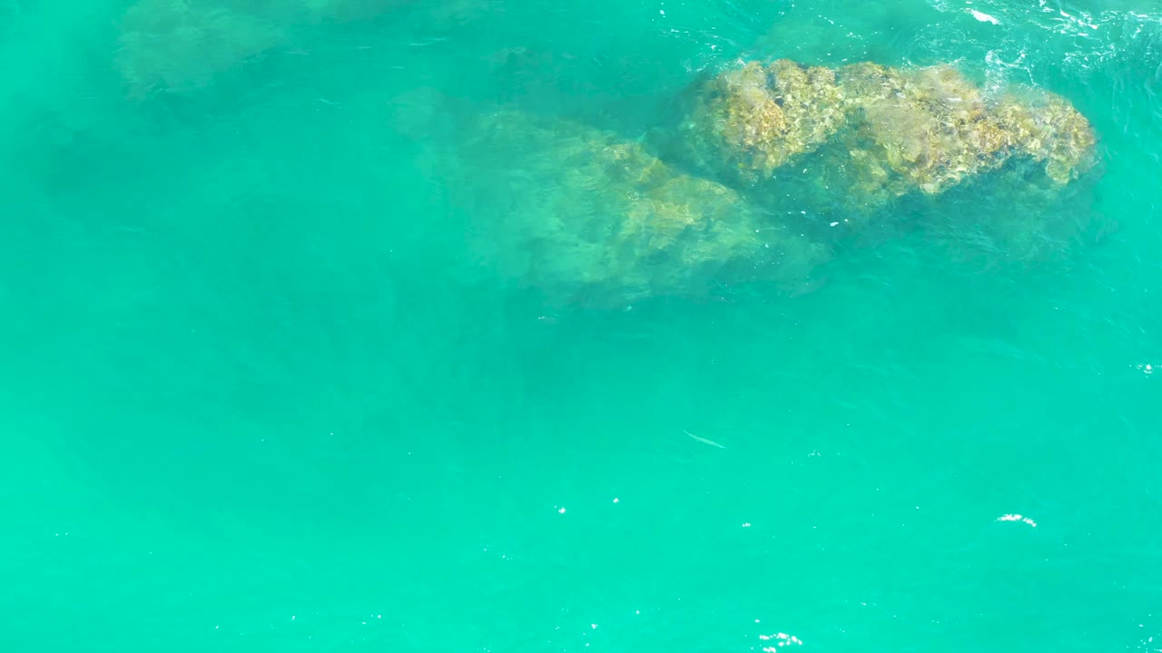 A larger submerged rock formation appears under bright turquoise water at Dreams Los Cabos, with gentle surface texture and no visible people.