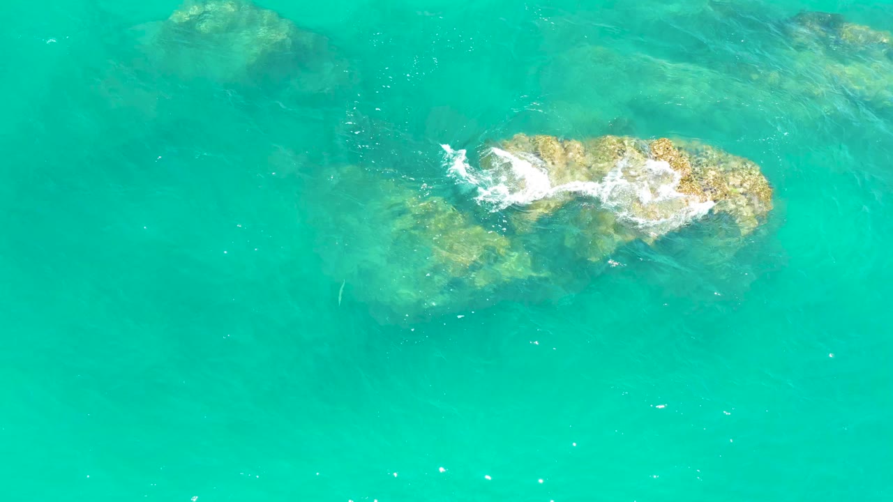 Turquoise water over submerged rocks with white foam