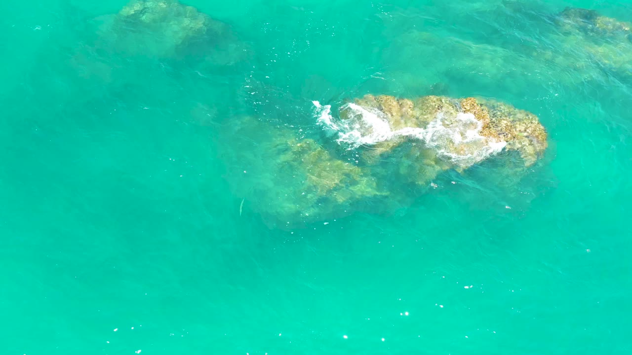 Overhead frame of transparent turquoise ocean at Dreams Los Cabos, Mexico, with the rock cluster slightly left of center under the surface and no visible people.