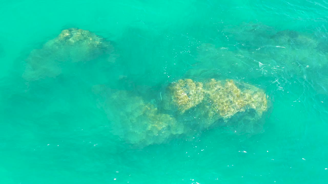 Overhead view of turquoise water at Dreams Los Cabos with submerged tan rocks near the upper and center frame and no visible people.
