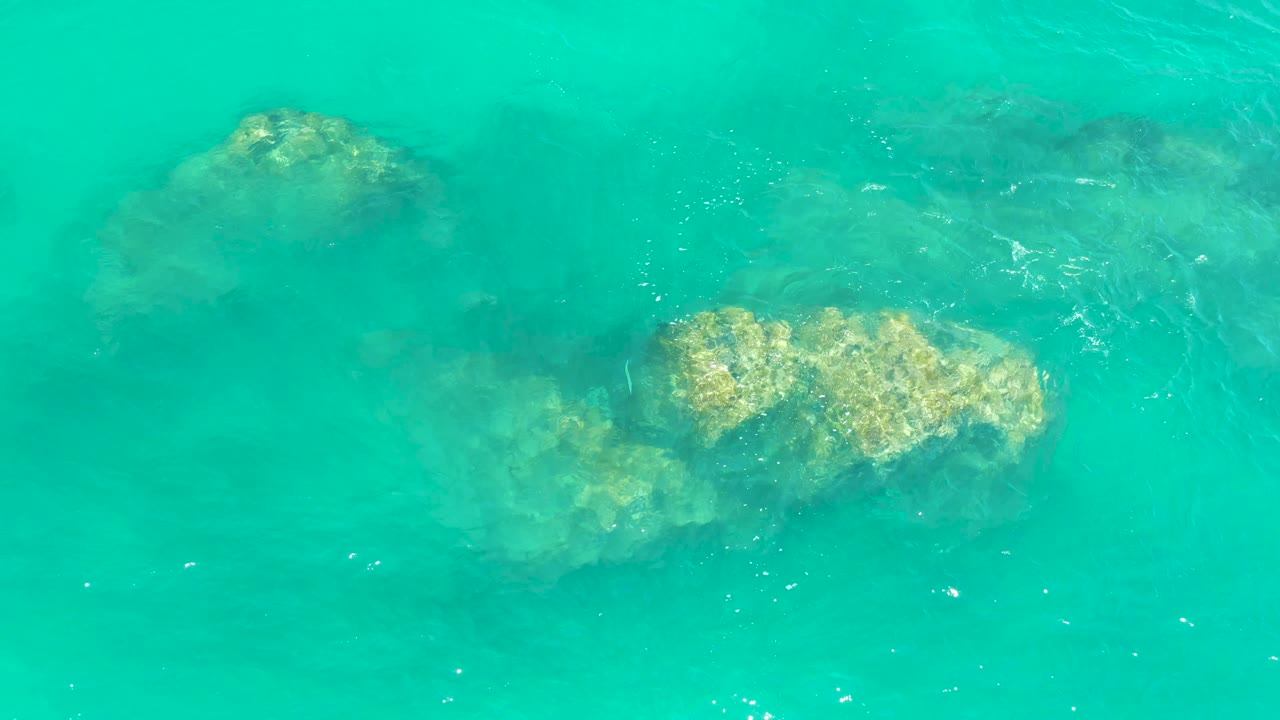 Turquoise sea covers several submerged rocks at Dreams Los Cabos, with the brightest rock mass centered right and no visible people.