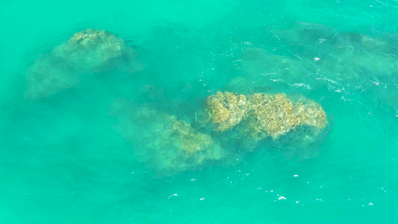 Clear turquoise water at Dreams Los Cabos reveals pale rocks in the middle and darker submerged forms behind them, with no visible people.