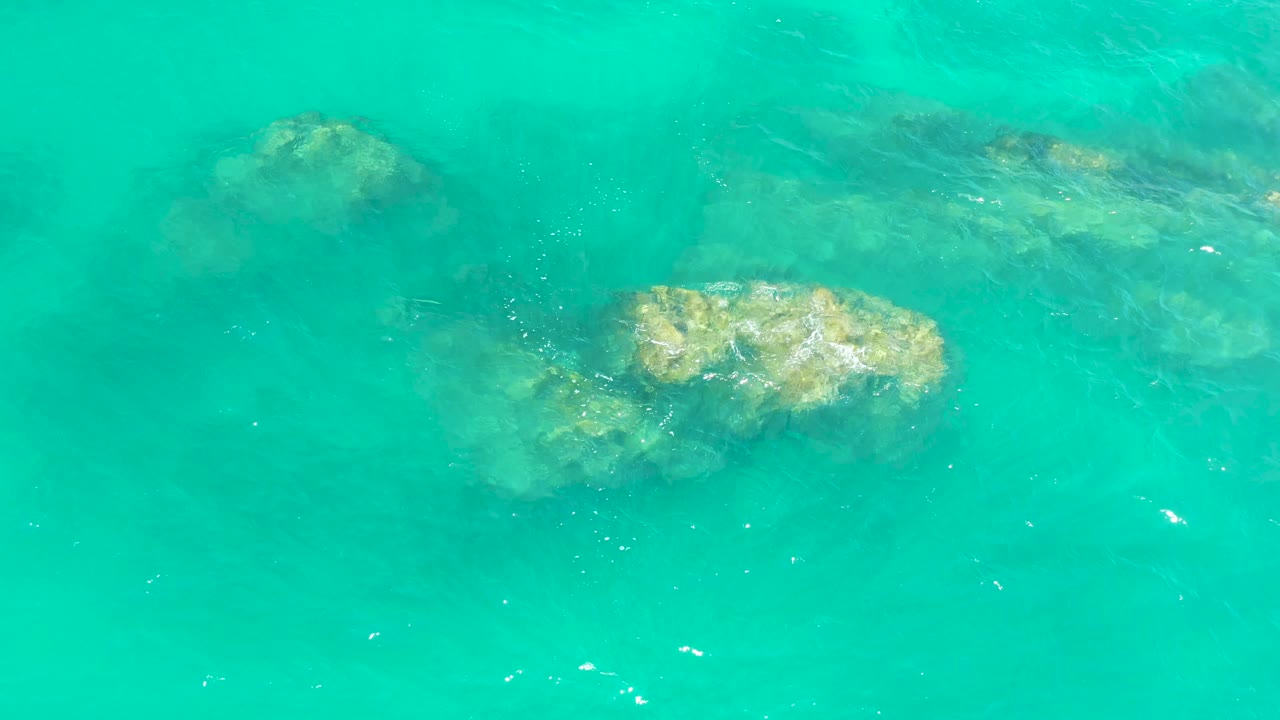Clear turquoise ocean at Dreams Los Cabos shows rock shapes beneath the surface with small white ripples crossing the center and no visible people.