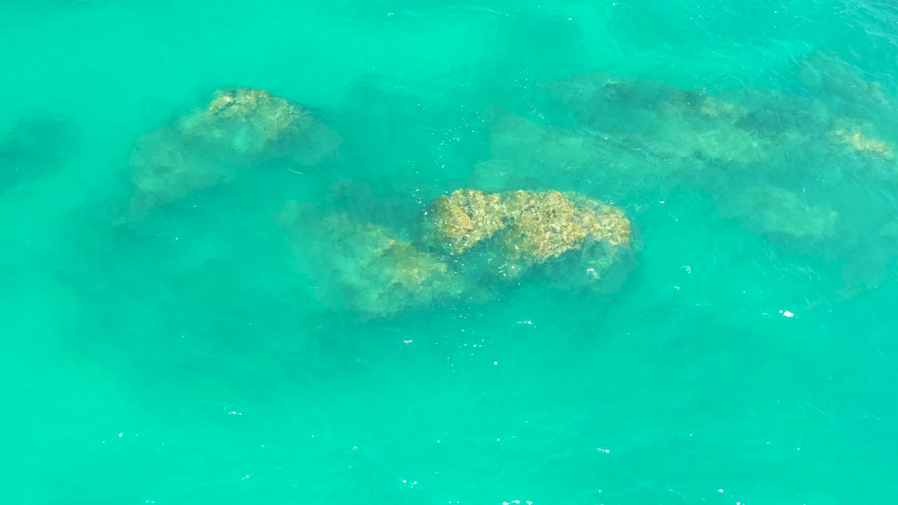Overhead view of turquoise water at Dreams Los Cabos with several submerged rocks visible beneath the surface and no visible people.