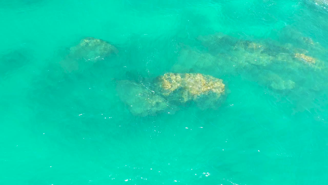 Clear rippled water reveals tan submerged rocks near the center of the frame at Dreams Los Cabos, with no visible people.