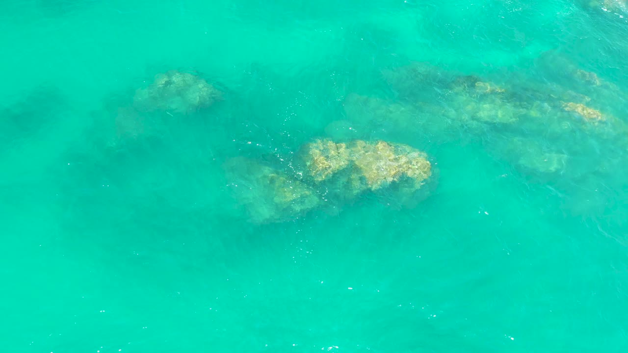 Bright turquoise shallow ocean water covers several underwater rocks at Dreams Los Cabos, Baja California Sur, with no visible people.