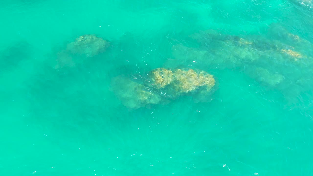 Submerged rock formations appear through green-blue water at Dreams Los Cabos as the surface texture softens the outlines, with no visible people.