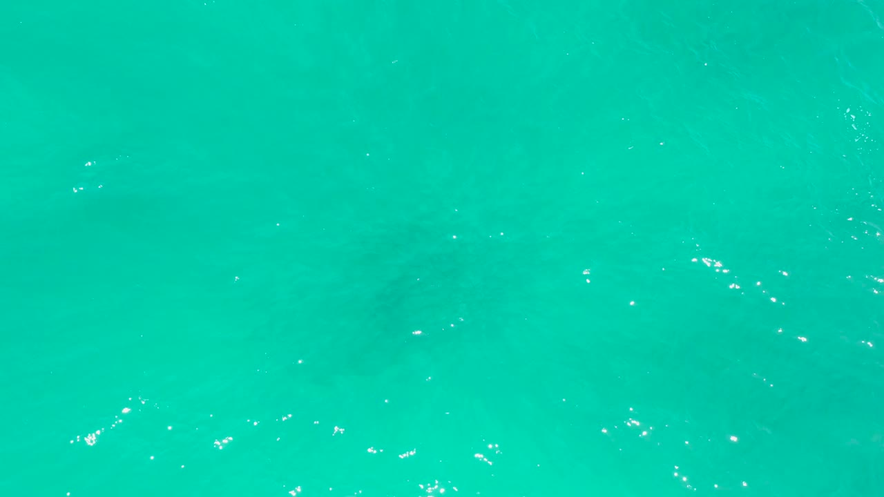 Clear turquoise ocean at Dreams Los Cabos with small foam flecks and a faint underwater shape beneath the surface, no visible people.
