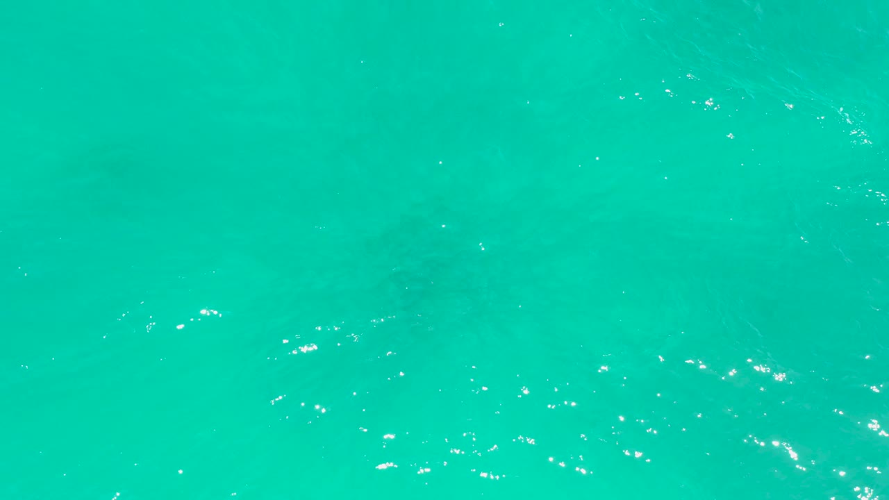 Overhead frame of turquoise ocean water at Dreams Los Cabos, with white specks on the surface and soft underwater haze, no visible people.
