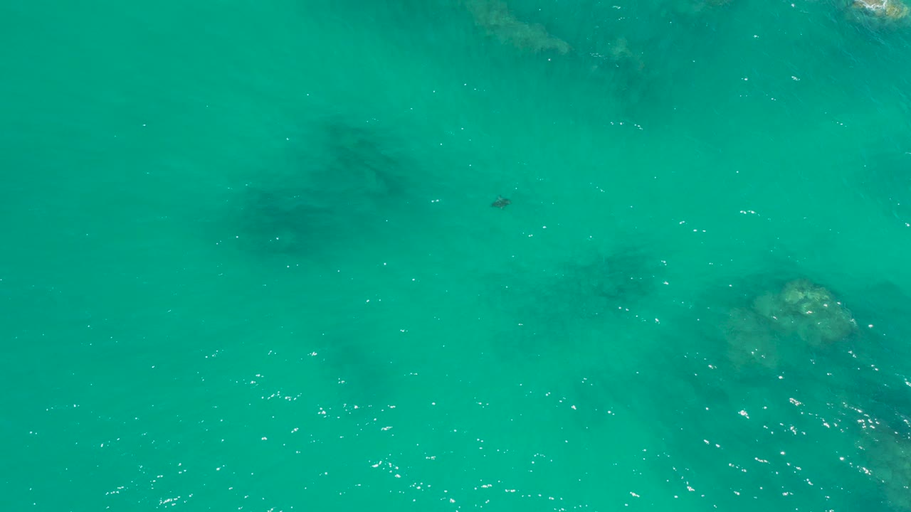 Turquoise sea surface at Dreams Los Cabos reveals a larger submerged rock form toward the lower right and no visible people.