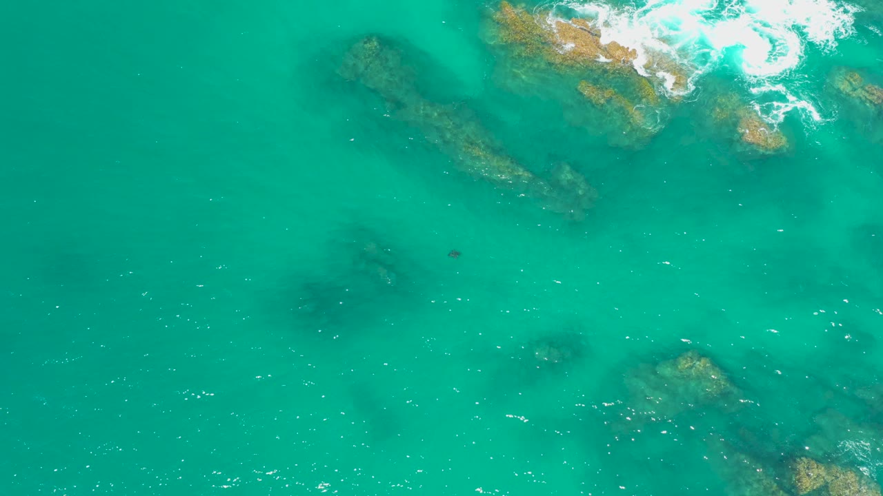 Aerial frame of clear turquoise water at Dreams Los Cabos, Mexico, with darker submerged rocks below the surface and no visible people.