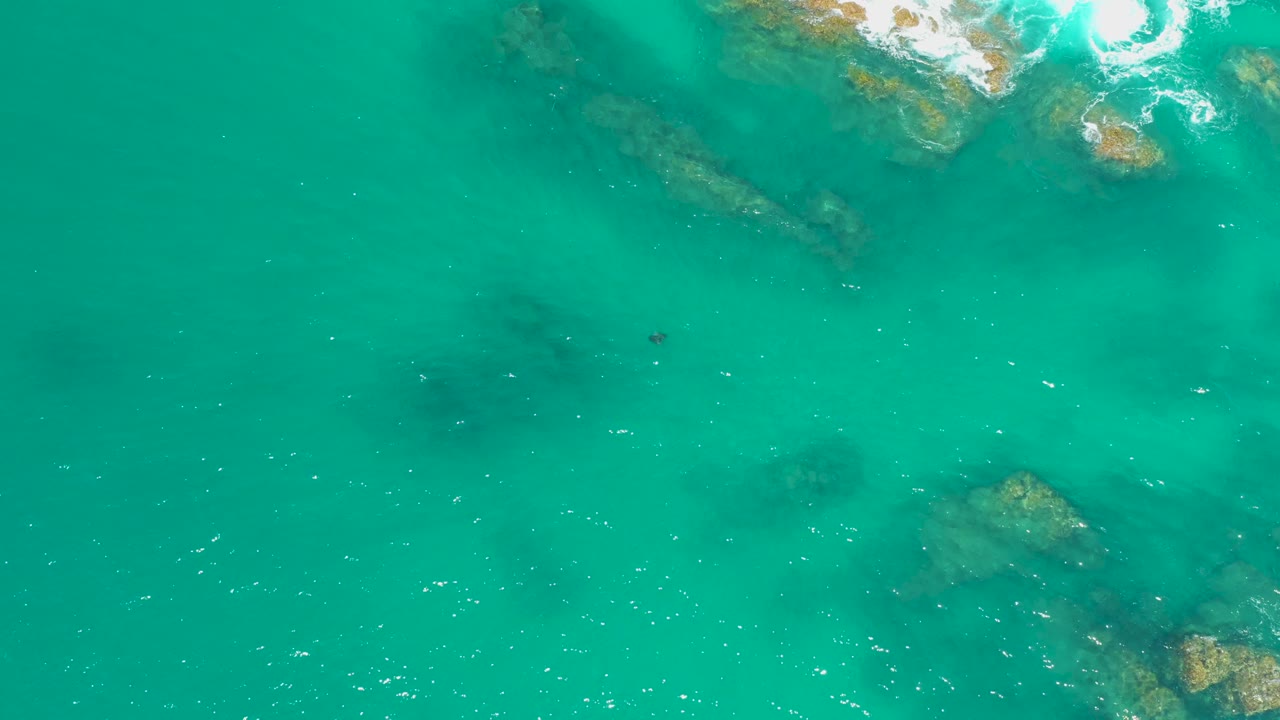 Aerial view of turquoise water at Dreams Los Cabos, Mexico, with rock clusters beneath the surface, a small foam patch near the top, and no visible people.