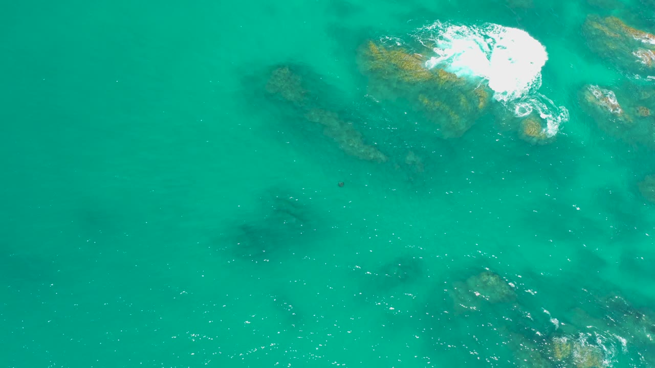 White wave foam spreading over brown submerged rocks in turquoise water.