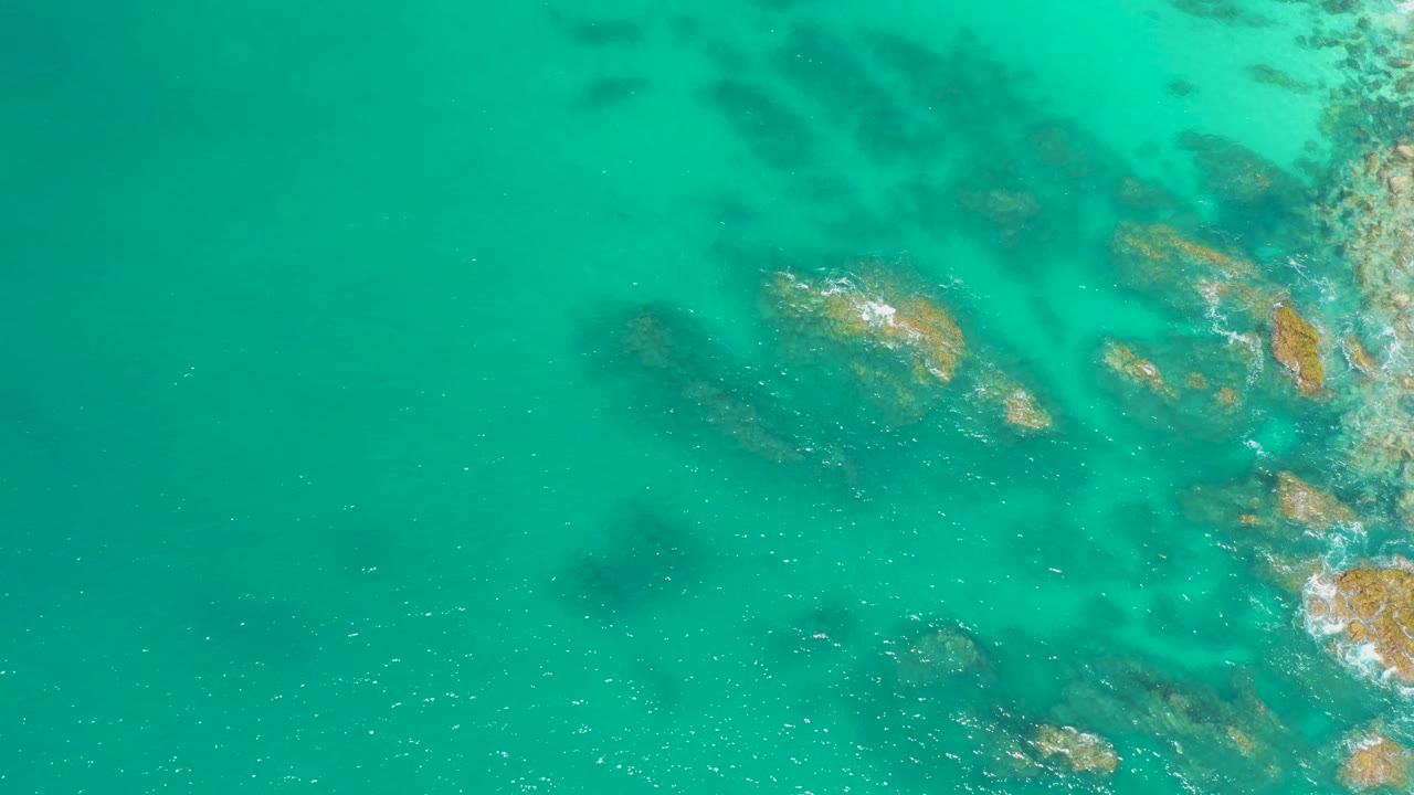 Overhead view at Dreams Los Cabos showing turquoise shallow water, submerged rocks, small white foam, and no visible people.