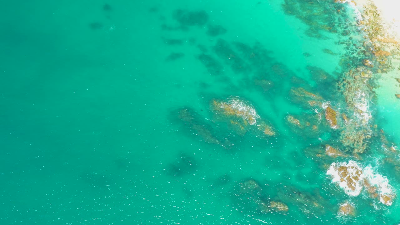 Overhead view of turquoise water and submerged rocks along the rocky edge at Dreams Los Cabos, Mexico, with small foam patches and no visible people.