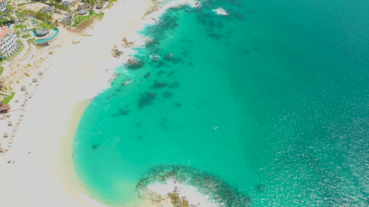 Aerial beach view with thatched umbrellas, white sand, and turquoise water.