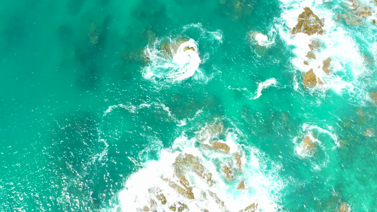 Turquoise sea with circular white foam around a rock.