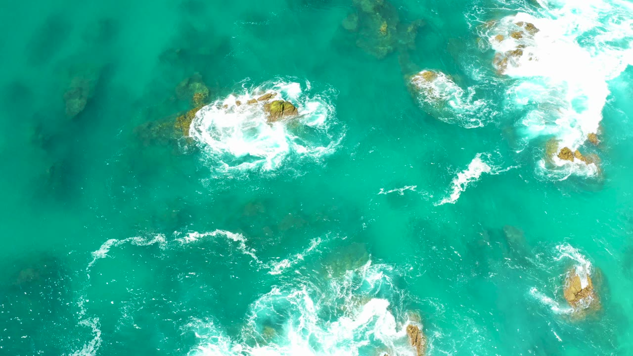 Overhead turquoise ocean water with white foam around rocks