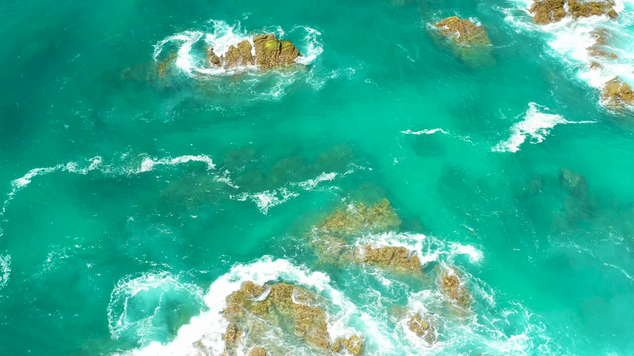 Turquoise ocean water with white waves around rocky outcrops