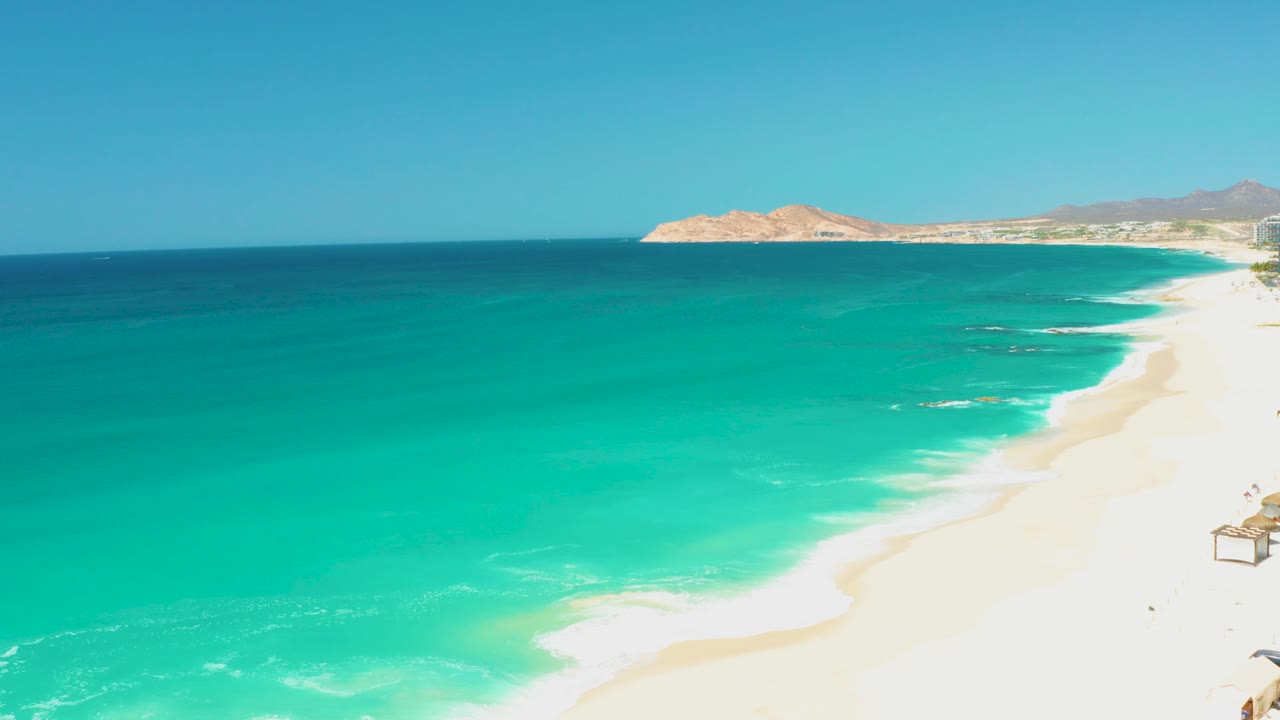 Diagonal sandy shore with teal ocean water and small white wave breaks.