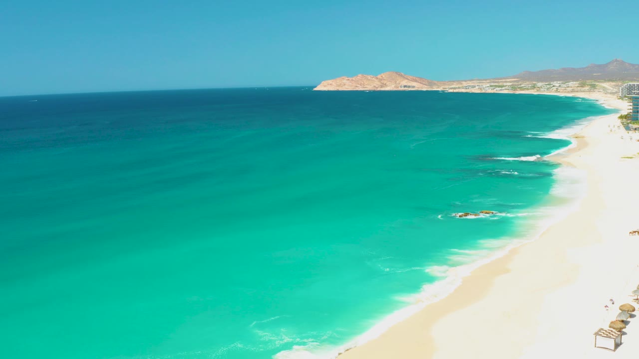 Fourth frame shows a broad turquoise water field, the sandy Dreams Los Cabos shore curving up the right side, low hills in the distance, and no visible people.