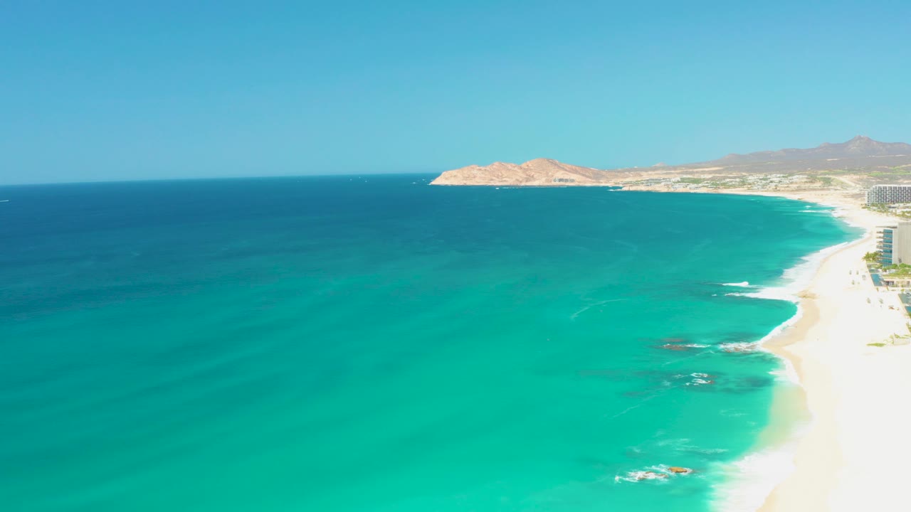 At 0:01, the Dreams Los Cabos beach curves along the right side while soft white wave lines appear over shallow turquoise water and no visible people are present.