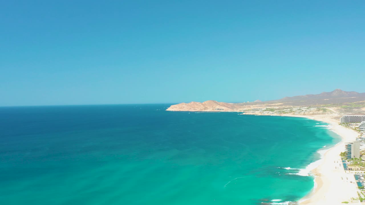 Wide coastline view with blue ocean, sandy shore, and distant mountains.