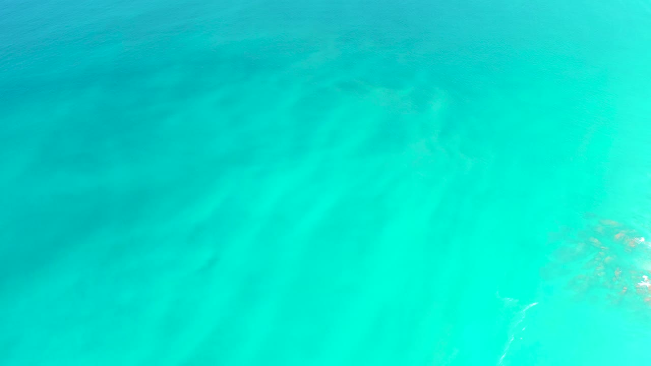 Turquoise ocean water with faint seabed detail and submerged vegetation near the right edge.