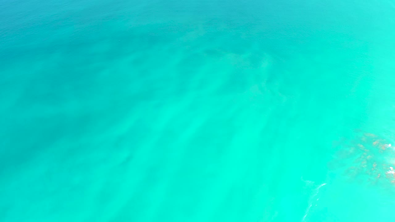 The second frame keeps the view on clear blue-green water at Dreams Los Cabos, with diffuse seabed patterns and tan vegetation still visible along the right side, with no visible people.