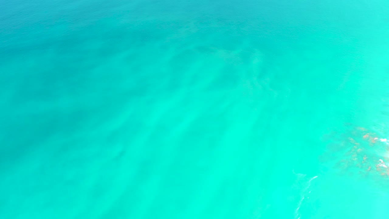 Midway through the clip, Dreams Los Cabos water remains shallow and clear, with soft ripple bands and submerged vegetation partly entering from the right, with no visible people.