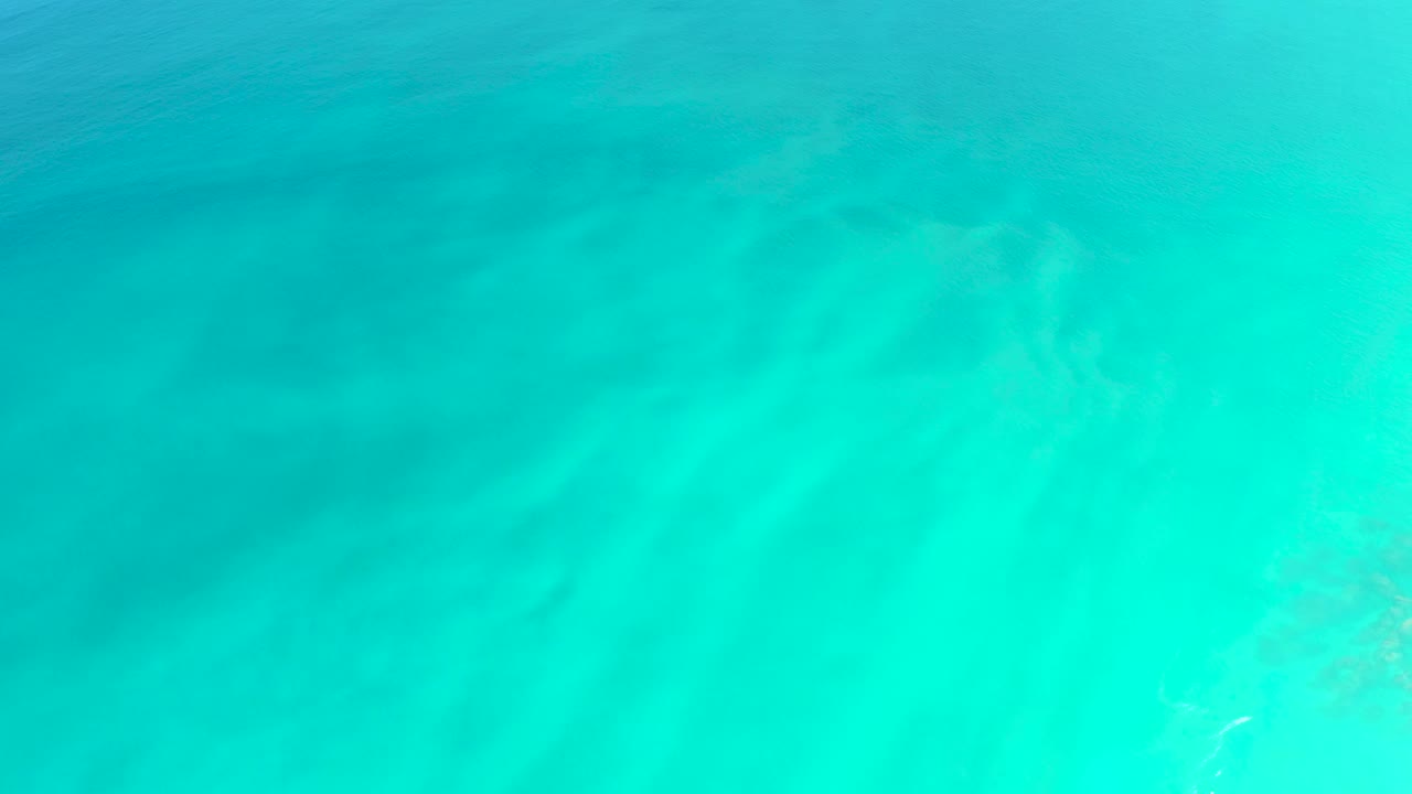 Clear shallow turquoise water covers muted sand detail at Dreams Los Cabos while the surface ripple pattern shifts, with no visible people.