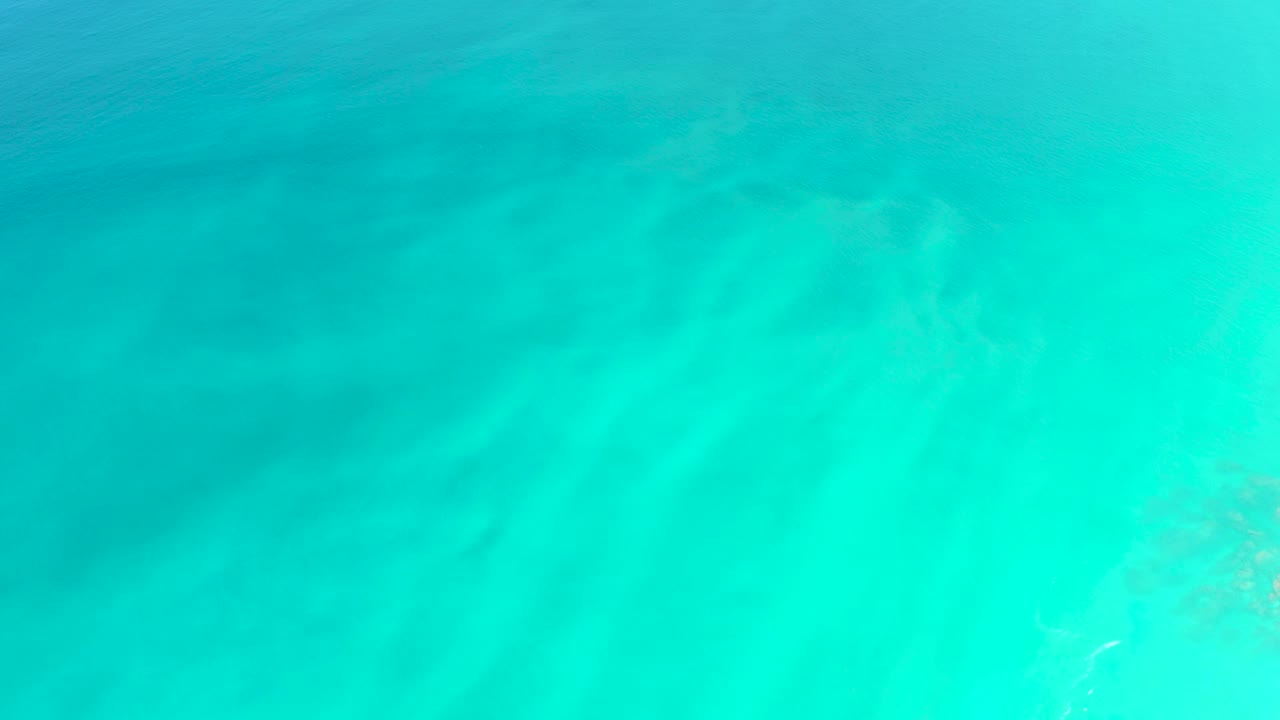 Bright turquoise water with faint sandy bottom texture.
