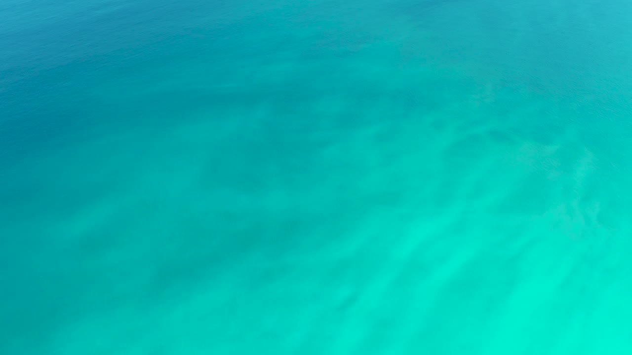 Shallow ocean water at Dreams Los Cabos shows darker submerged areas beneath a smooth turquoise surface and no visible people.