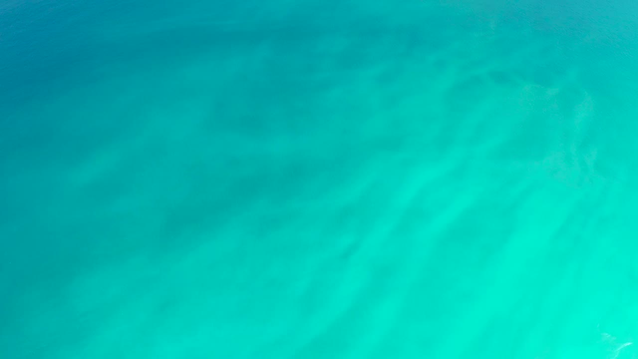 Calm blue-green water at Dreams Los Cabos reveals a sandy bottom with soft cloudy tonal bands and no visible people.