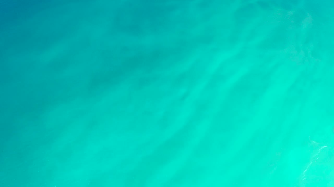 Bright turquoise water at Dreams Los Cabos shows faint underwater texture and delicate ripple bands, with no visible people.