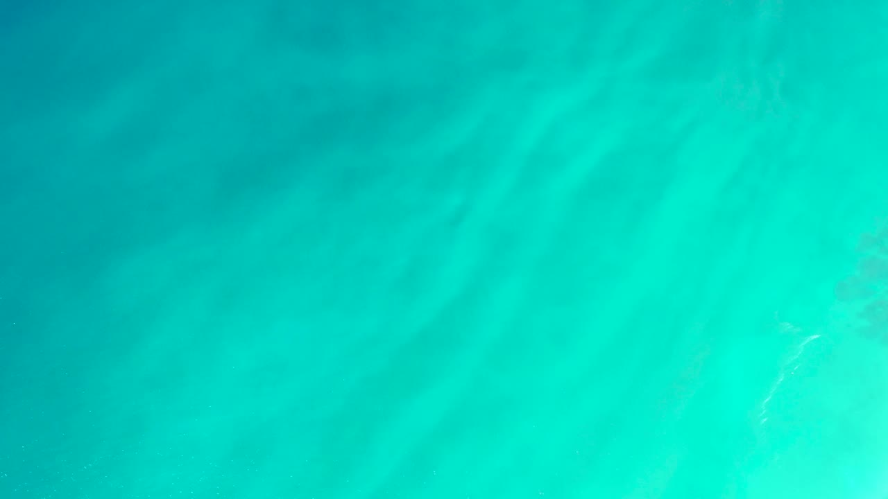 Top-down view of turquoise ocean water over pale sand ripples at Dreams Los Cabos, with no visible people.