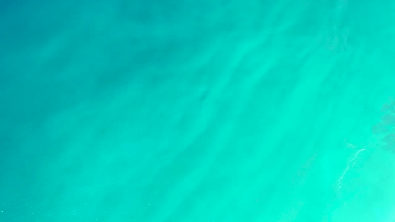 Clear blue-green ocean water fills the frame with faint sand patterns visible below the surface, no visible people.