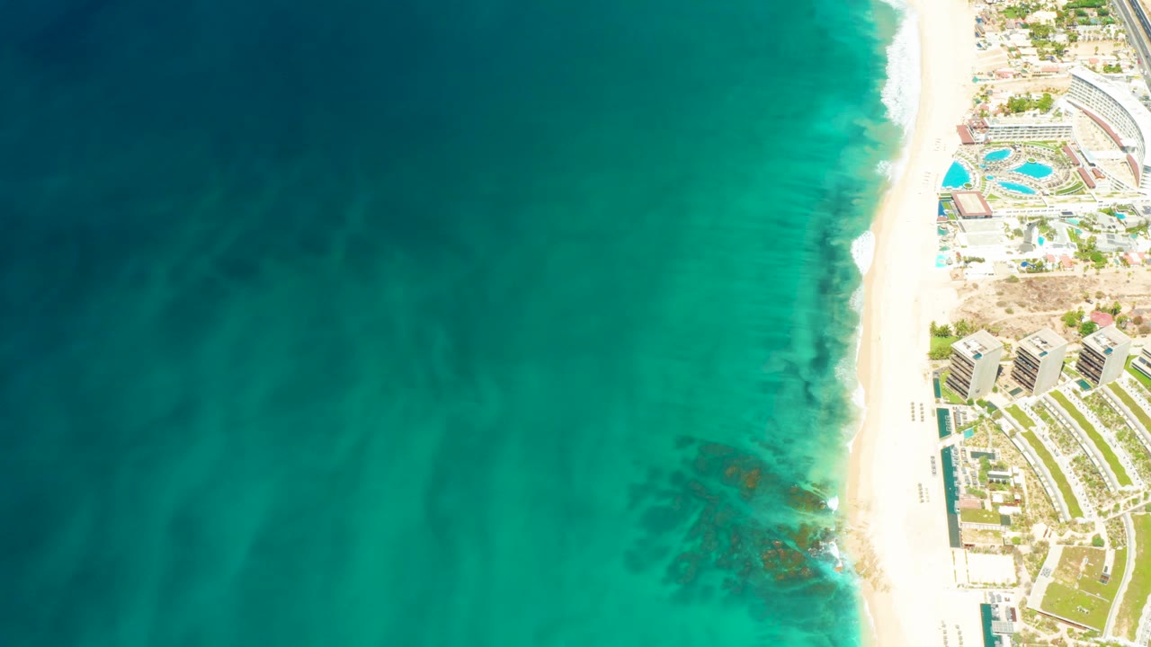 Overhead turquoise ocean beside a white beach and resort grounds