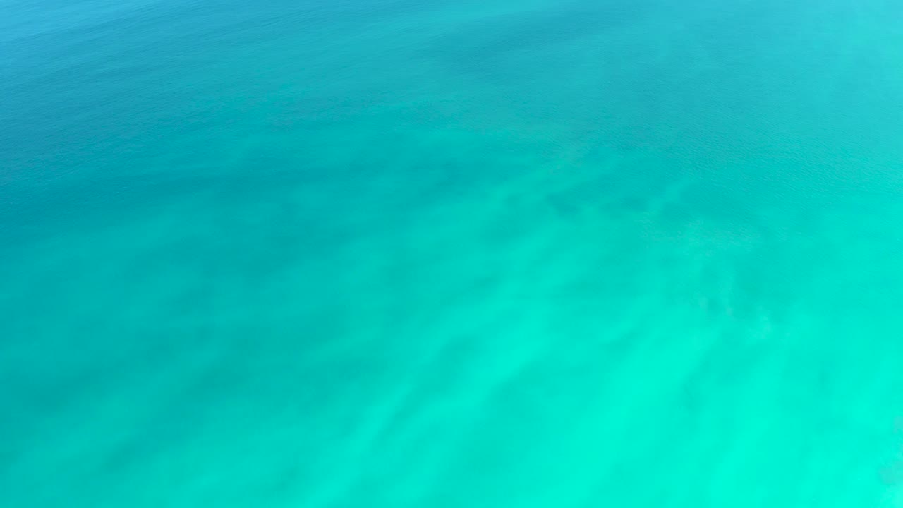 Clear turquoise shallow ocean water over a pale sandy bottom at Dreams Los Cabos, with faint surface ripples and no visible people.