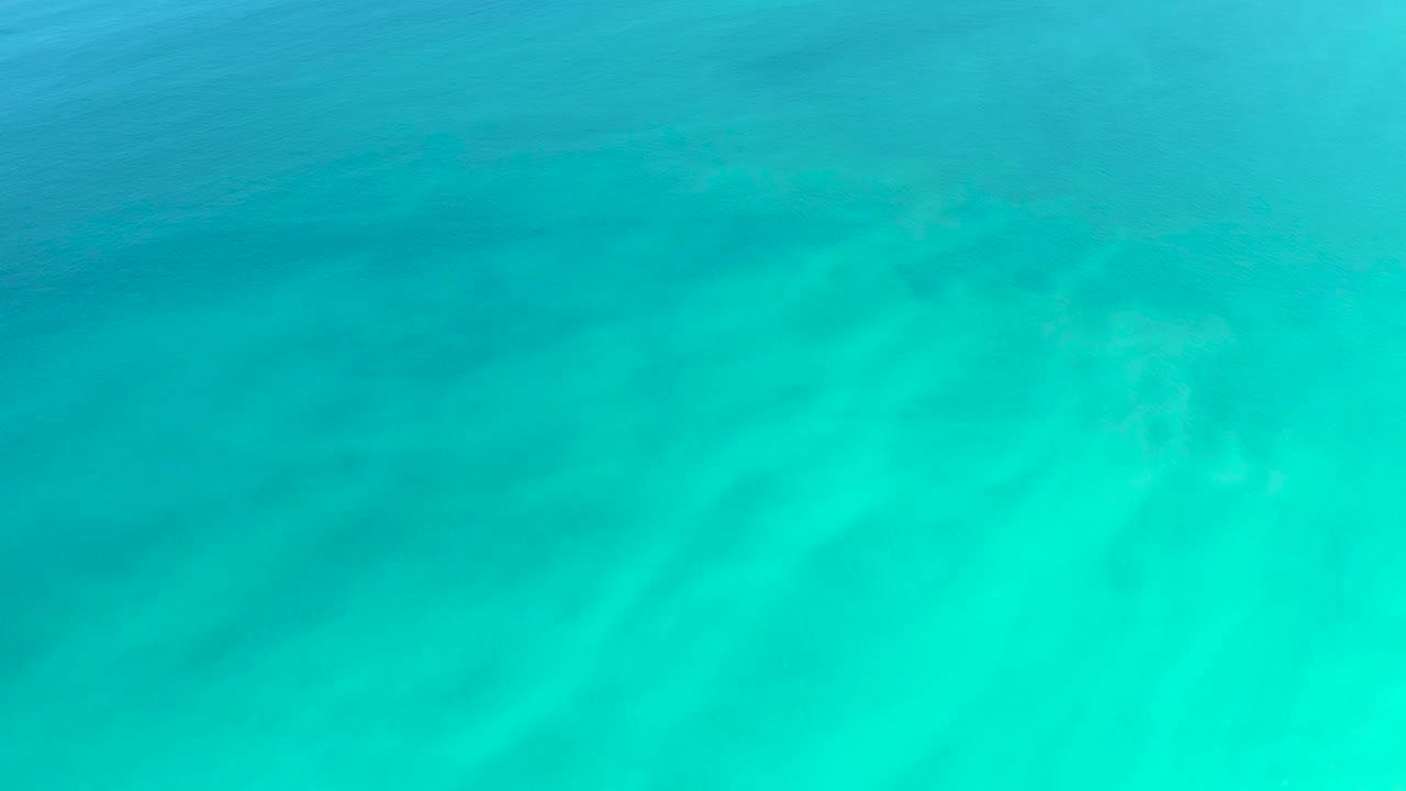Clear teal ocean water at Dreams Los Cabos shows darker ripple bands crossing the sandy bottom, with no visible people.