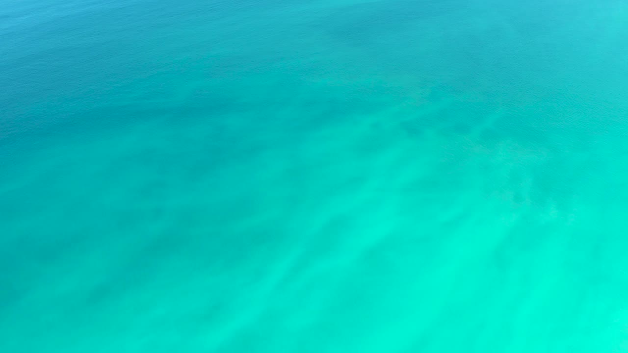 Downward aerial-style view of turquoise ocean at Dreams Los Cabos, with subtle surface ripples over sandy seafloor and no visible people.