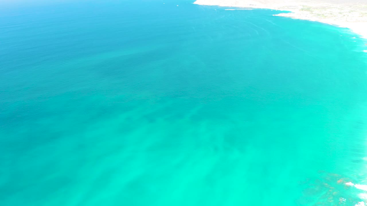 Aerial view of turquoise ocean water near Dreams Los Cabos with a pale sandy shoreline along the upper right edge and no visible people.