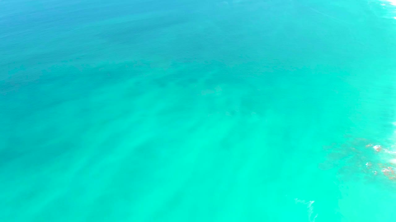 Blue-green shallow water at Dreams Los Cabos shows faint sand and darker underwater shapes with no visible people.