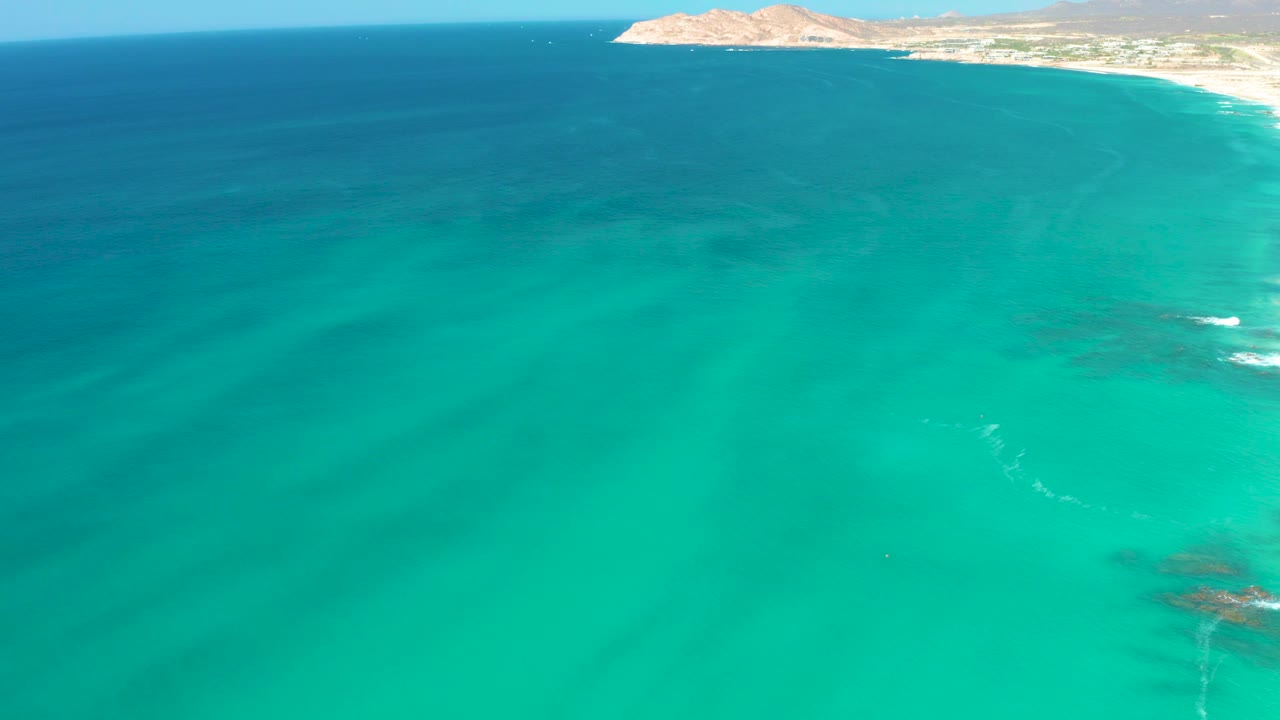 Aerial view of turquoise ocean beside a distant shoreline and hill.