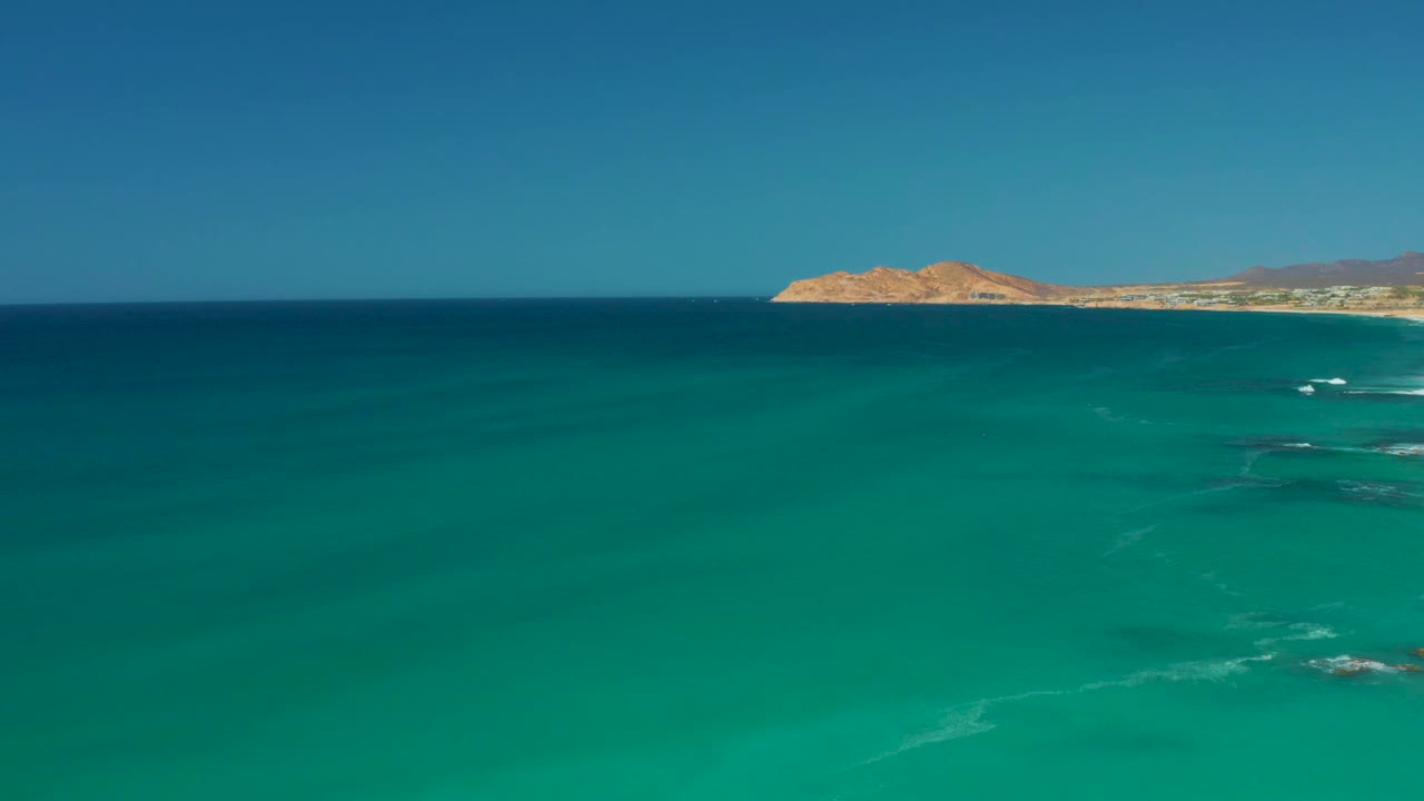 Turquoise ocean with distant sandy coastline and blue sky.