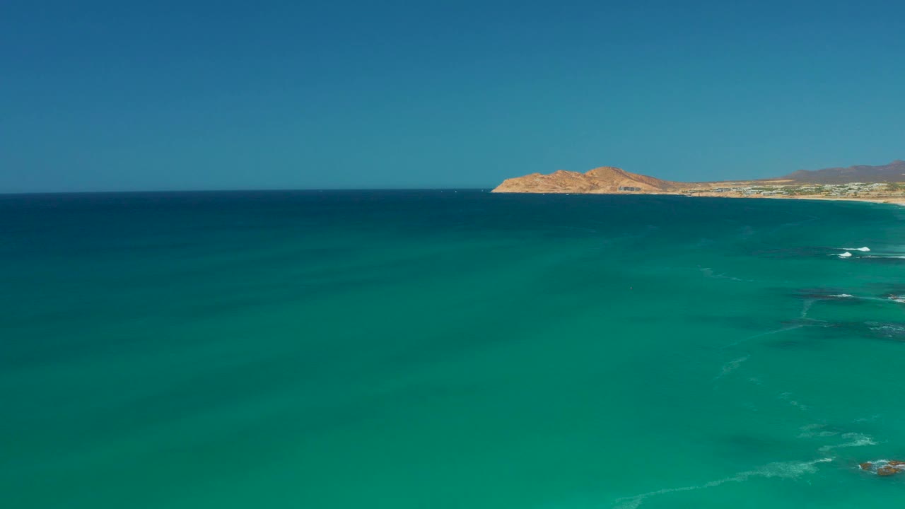 The ocean surface shows darker submerged patches below the turquoise water, with the Dreams Los Cabos coastline sitting high in the frame and no visible people.