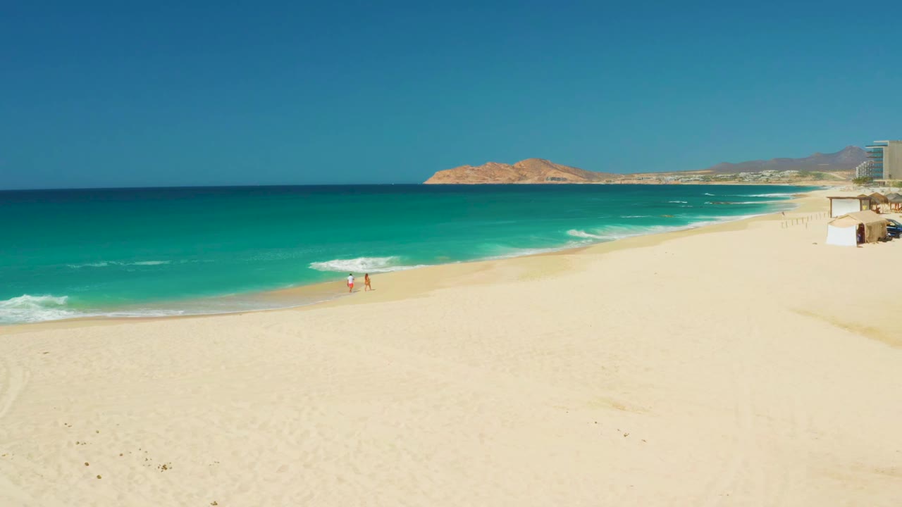 Open beach and ocean waves with two people walking along the shoreline.