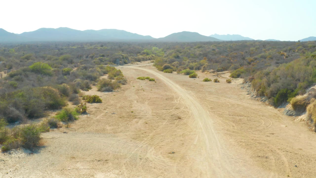 Dry road corridor with scrub on both sides and mountains beyond
