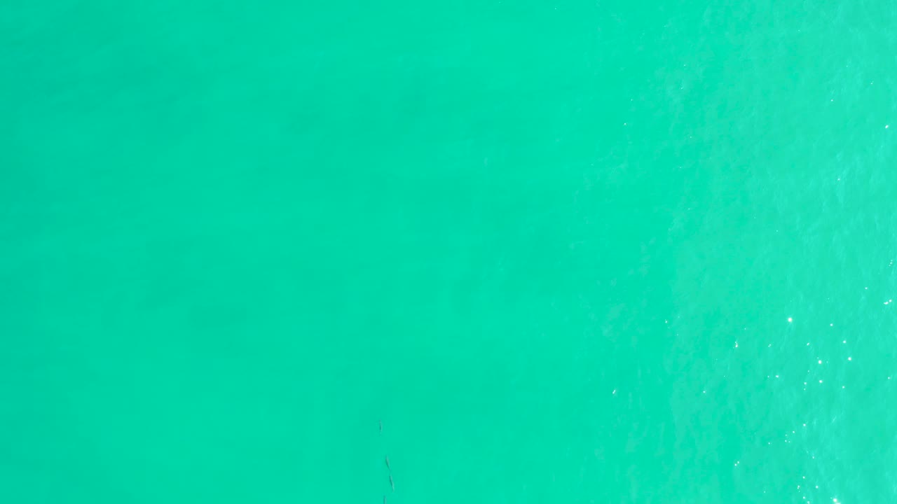 Aerial-looking turquoise sea surface in Los Frailes, Baja California Sur, with a soft foamy band on the right and no visible people.