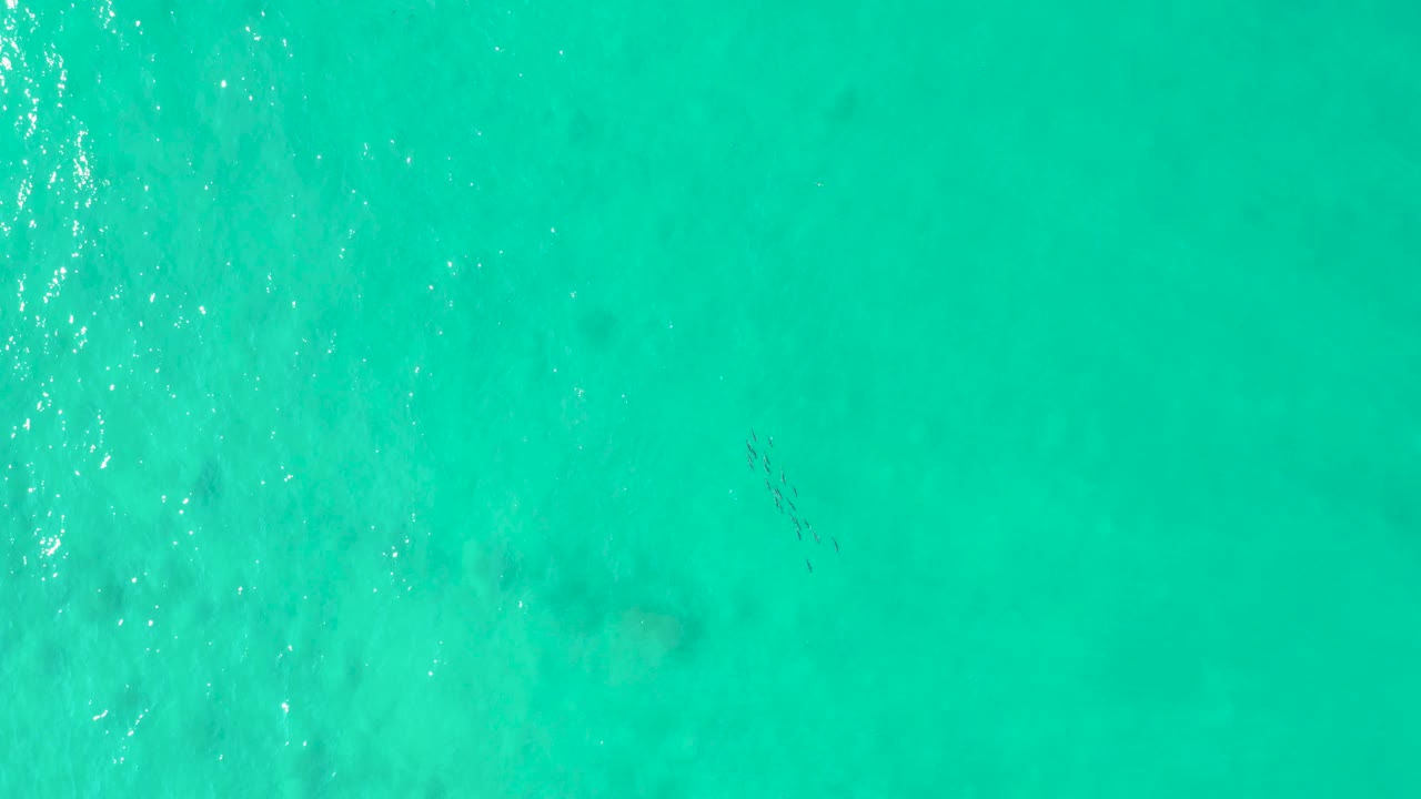 Overhead Los Frailes ocean view with smooth turquoise water, pale seabed variations, faint darker underwater marks, and no visible people or vessels.